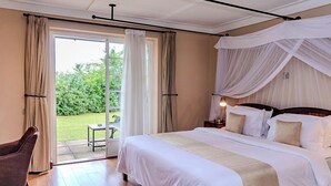Une chambre avec un grand lit, une chaise et une vue sur le jardin, accessible par une porte vitrée.