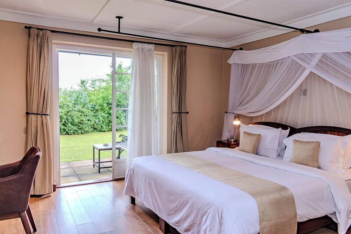A bedroom with a large bed, a chair, and a view of the garden through a glass door.