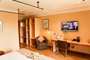 A hotel room with a bed, a desk, a chair, a television, and a bookshelf. - Aero Club of East Africa (Nairobi)
