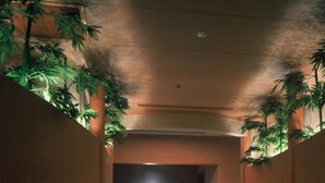 A corridor with a stone floor, wooden pillars, and green plants. - Aeria Tohno (Tono)