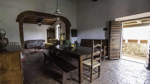 A rustic dining area with a wooden table and benches, a hanging light fixture, and a stone wall in the background. -  Padronale house apartment Fontaccia (Montiano)