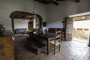 Un coin repas rustique avec une table et des bancs en bois, un luminaire suspendu et un mur de pierre en arrière-plan.