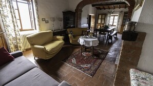 A cozy living room with a sofa, armchair, and a small table with a tablecloth. There is a patterned rug on the floor, and a window with curtains. -  Padronale house apartment Fontaccia (Montiano)