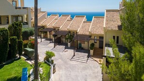 Un complejo turístico con varias edificaciones, una zona de piscina y vistas al mar.
