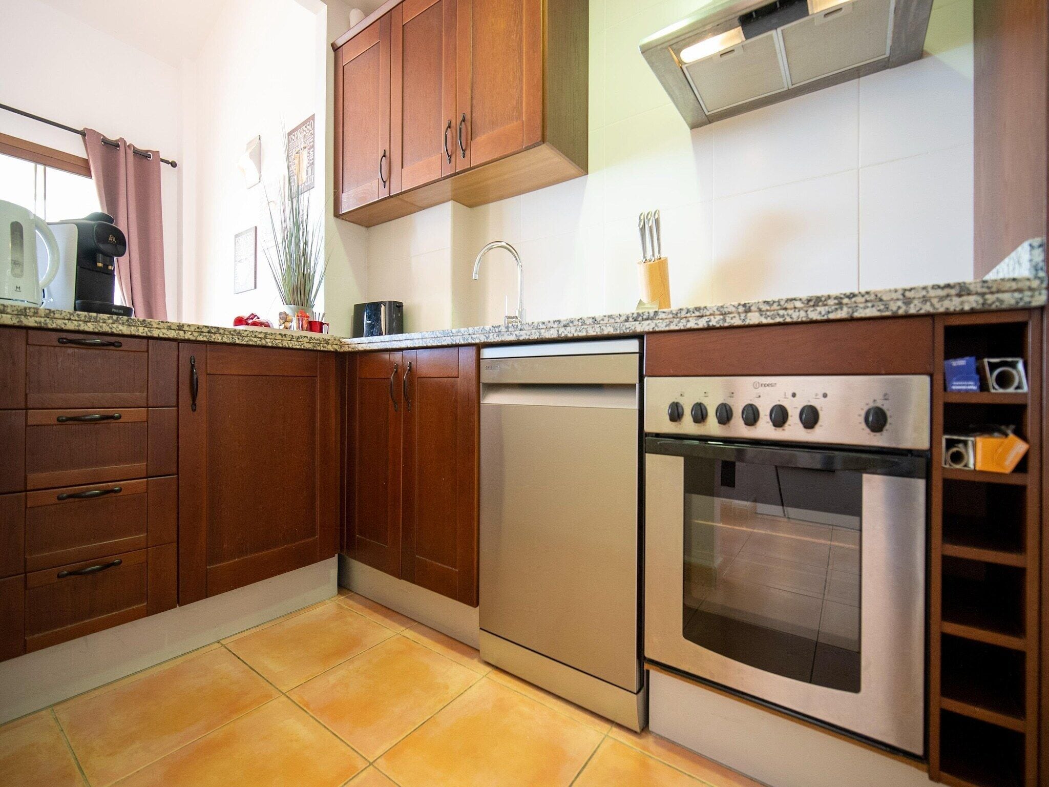 Uma cozinha com armários de madeira, máquina de lavar louça, forno e bancada de granito.