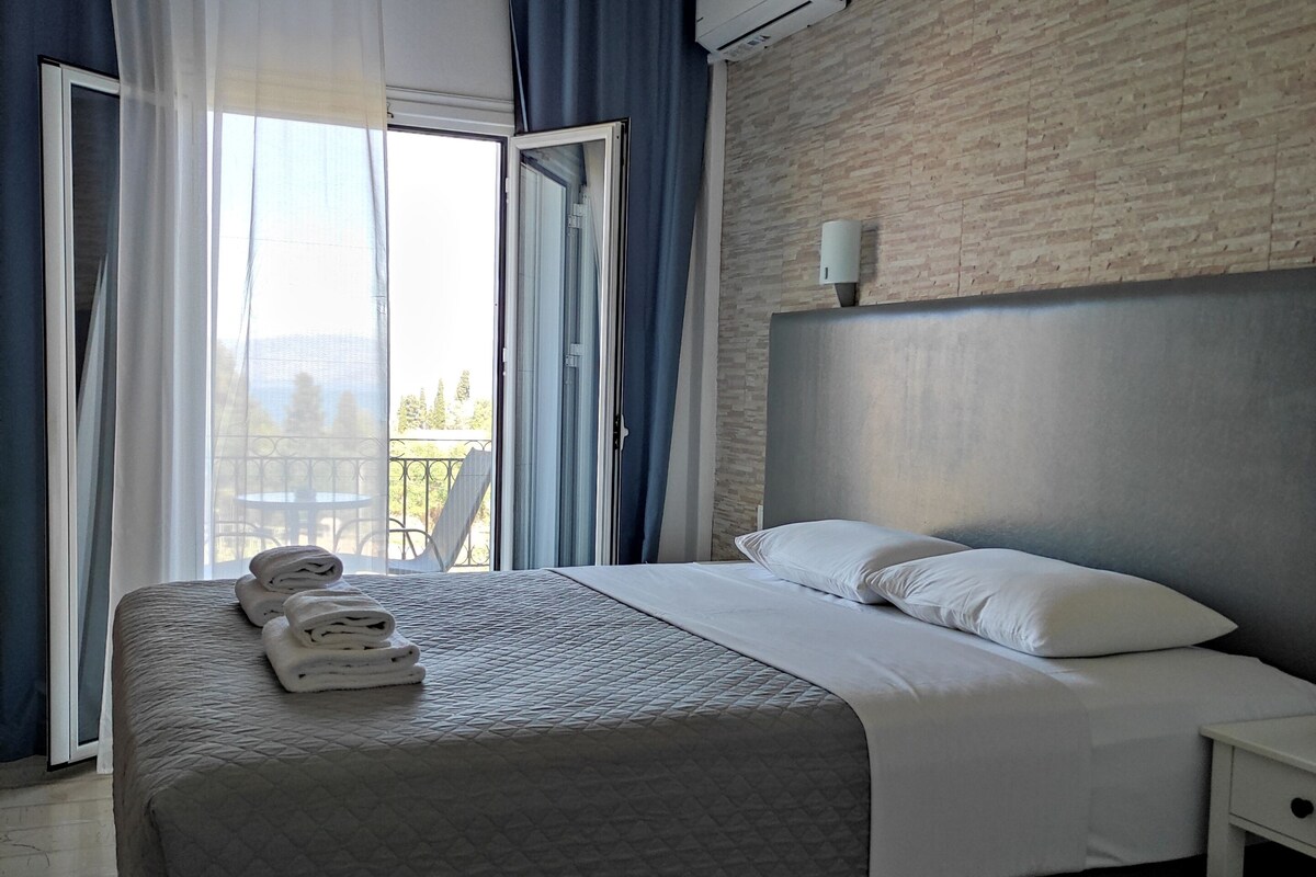 Une chambre d’hôtel moderne, équipée d’un lit, d’une table de chevet, d’un climatiseur fixé au mur et offrant une vue à travers une porte vitrée.
