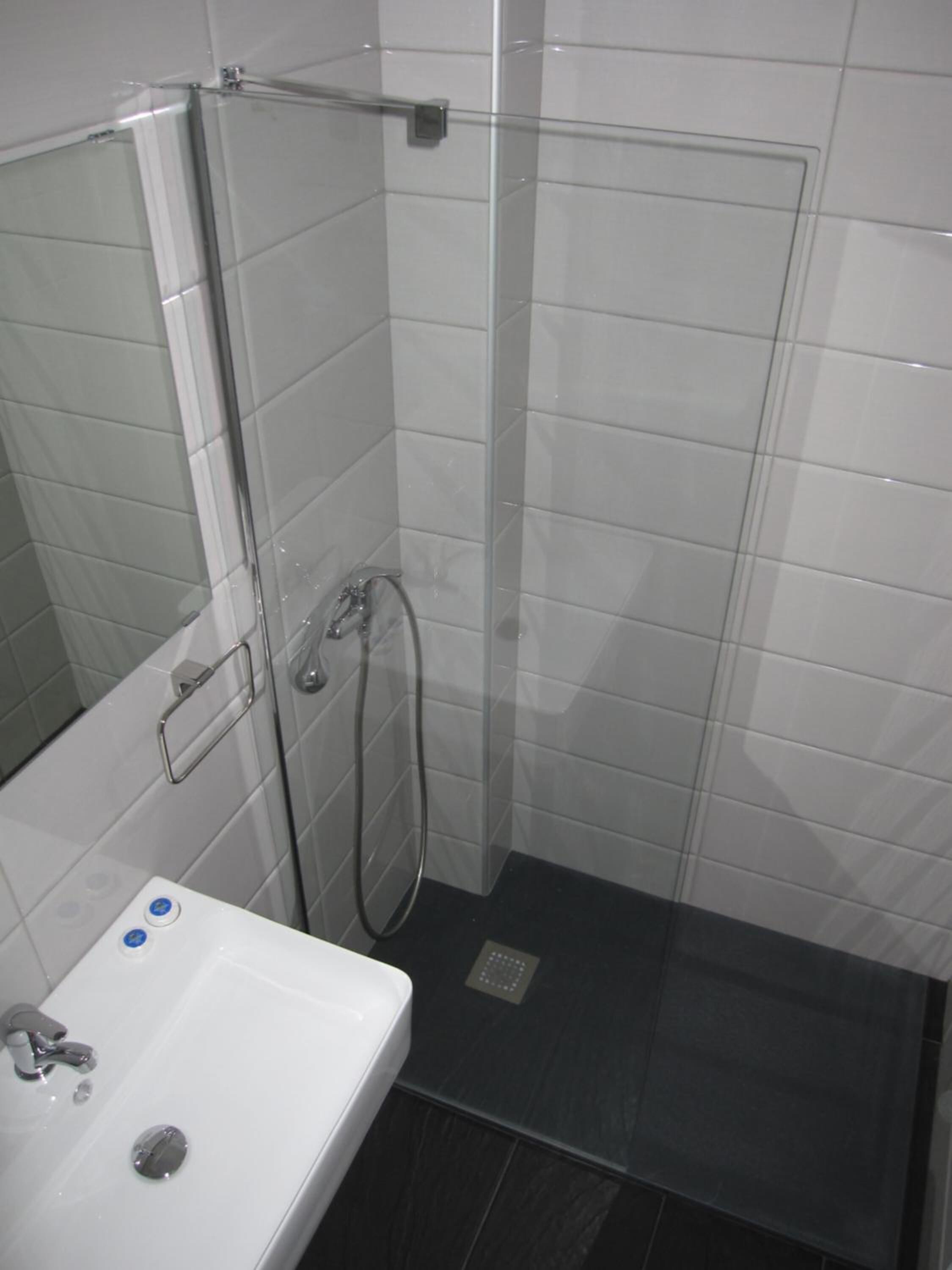Une salle de bain avec un lavabo blanc, une douche en verre et un sol carrelé.