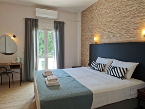 A hotel room with a bed, a desk, a chair, a mirror, and an air conditioning unit. - Hotel Tina (Corfu)
