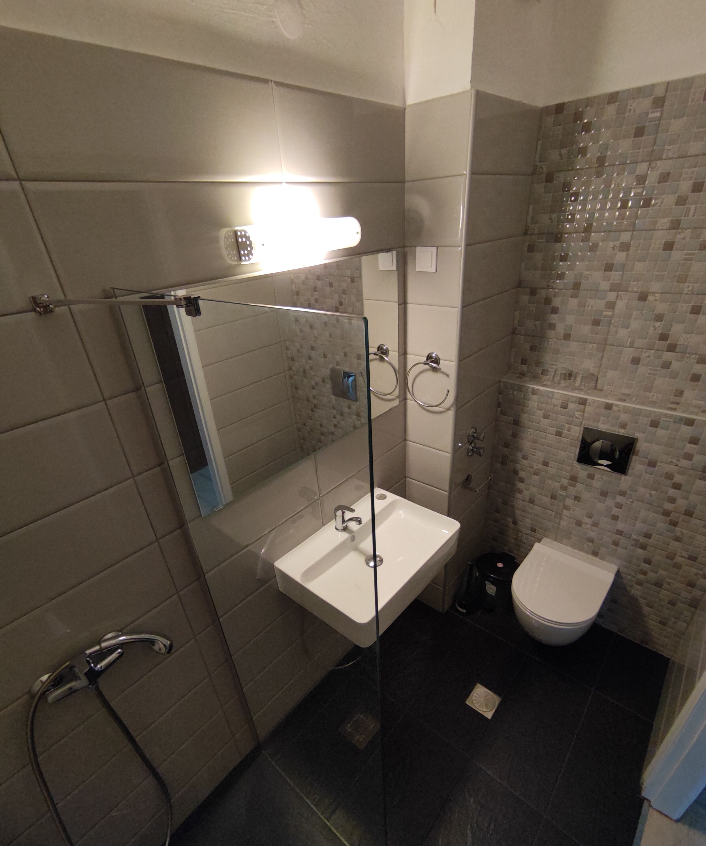 Une salle de bain avec une douche à parois de verre, un lavabo blanc, des toilettes et un miroir.