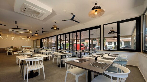 A spacious restaurant with white chairs and tables, large windows, and ceiling fans. - Hotel Tina (Corfu)