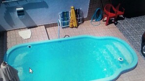 A swimming pool with a tiled deck, a red chair, and a yellow umbrella. - Beach house in Boissucanga * Carnival, Easter, and other holidays* (Praia de Boiçucanga)