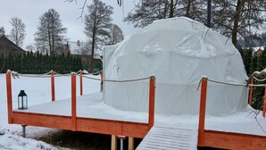 Lumipeitteinen iglu, jonka edessä on puinen alusta ja kaide.