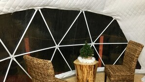 Mukava oleskelualue, jossa on rottinkituoleja ja pieni puinen pöytä. Alue sijaitsee suuren ikkunan edessä, ja ikkunassa on geometrinen kuvio.