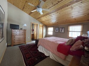 A bedroom with a bed, a dresser, a ceiling fan, and a window.