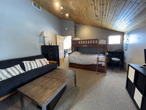 A room with bunk beds, a sofa, a desk, and a lamp.