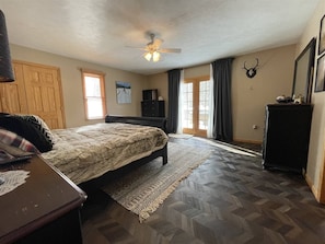 A bedroom with a bed, a desk, a dresser, a ceiling fan, and a window with curtains.