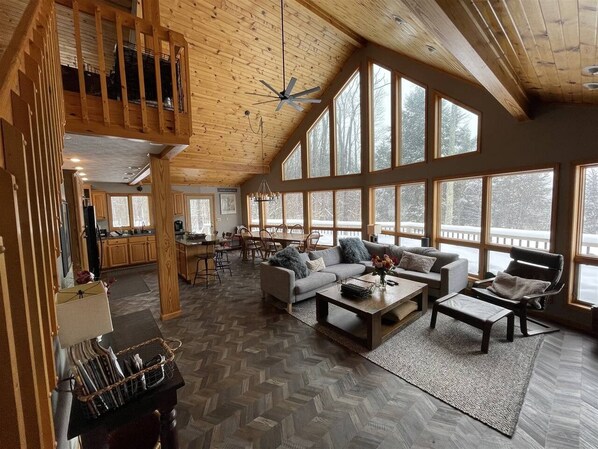 A spacious living area with a herringbone floor, large windows, and a loft with a wooden staircase.