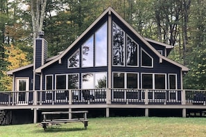 A two-story cabin with a balcony and a chimney, surrounded by trees.