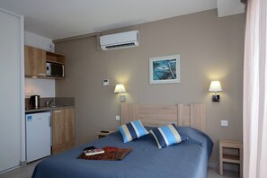 A hotel room with a bed, bedside lamps, a painting, a microwave, and a small kitchenette.