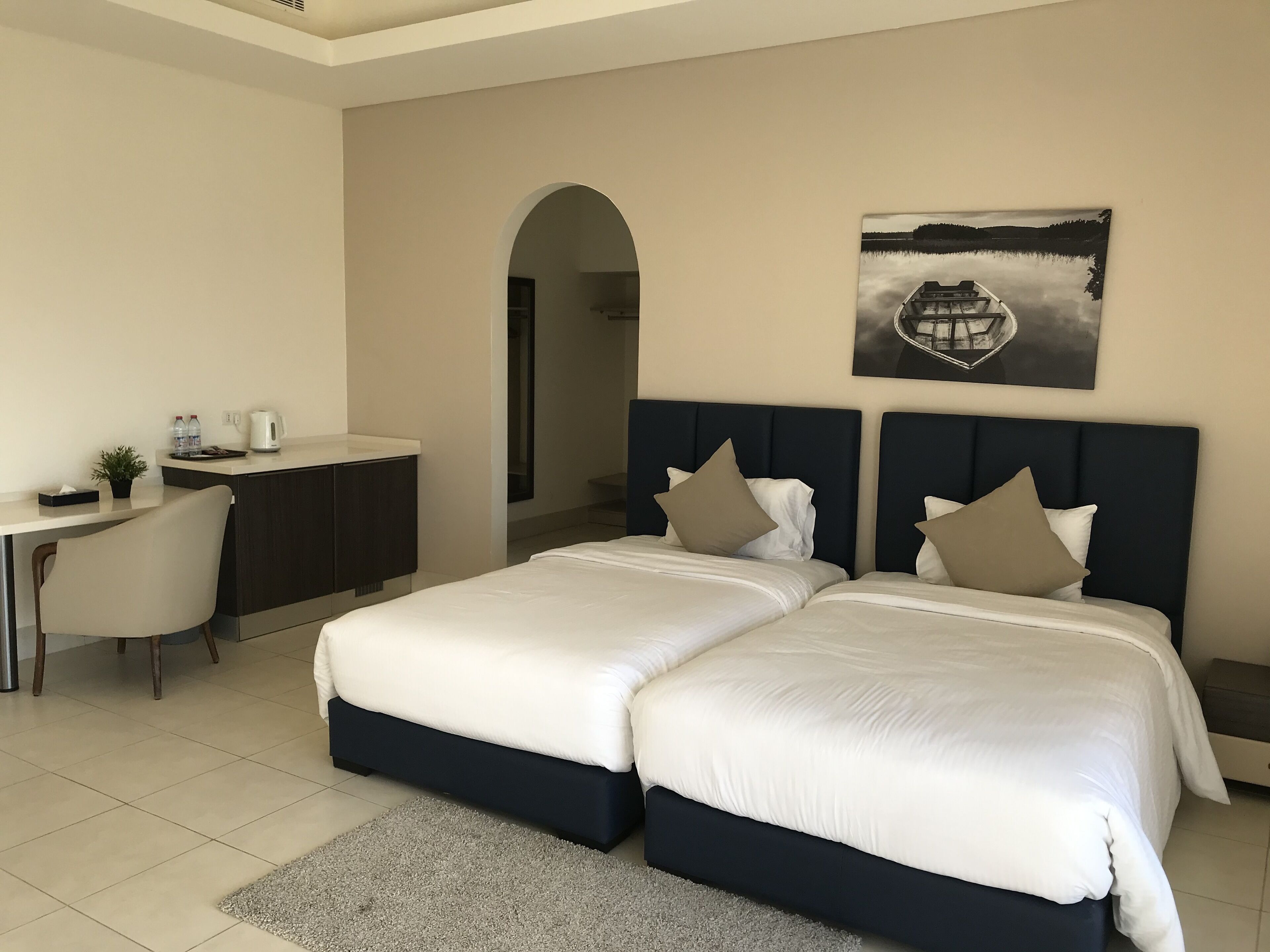 Habitación de hotel con dos camas, un escritorio, una silla, una cafetera y un cuadro en la pared.