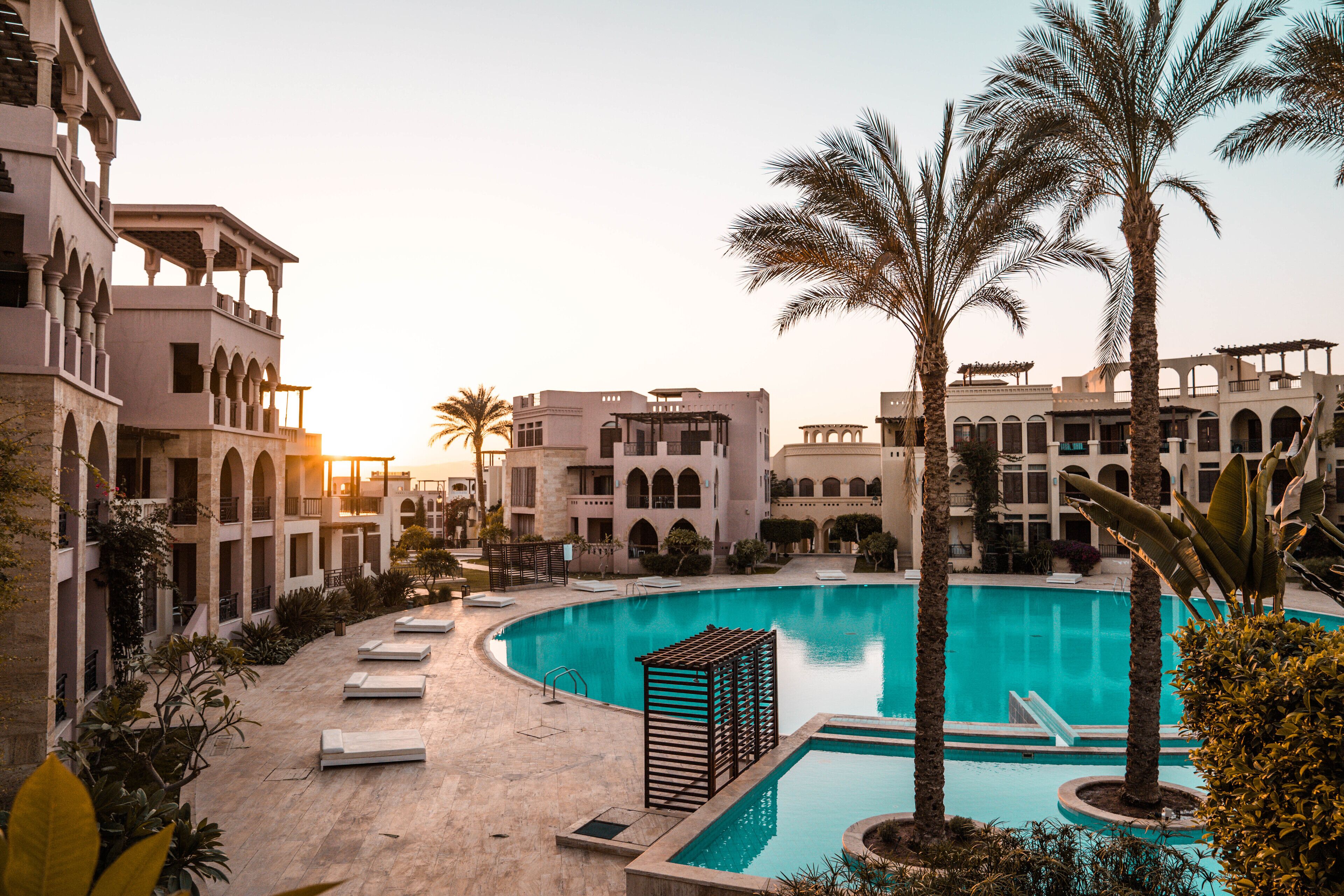 A pool area with a large central pool, surrounding lounge chairs, and palm trees.