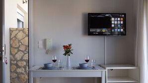 En matplats med ett bord dukat för två personer, en vas med blommor och en tv som är monterad på väggen och visar en väderapp.