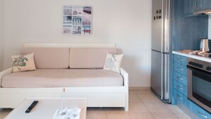 Ett kompakt bostadsutrymme med en soffa, ett litet bord, ett kylskåp och en köksdel.