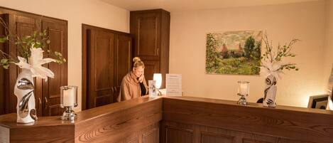 A reception desk with wooden paneling, a framed landscape painting on the wall, and a vase with white flowers.