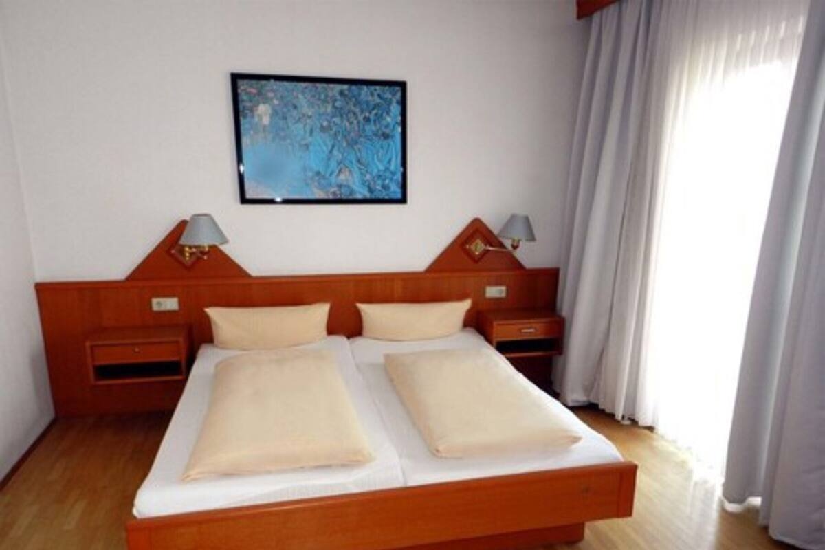A double bed with two pillows, wooden headboard, nightstands with lamps, and a painting on the wall.