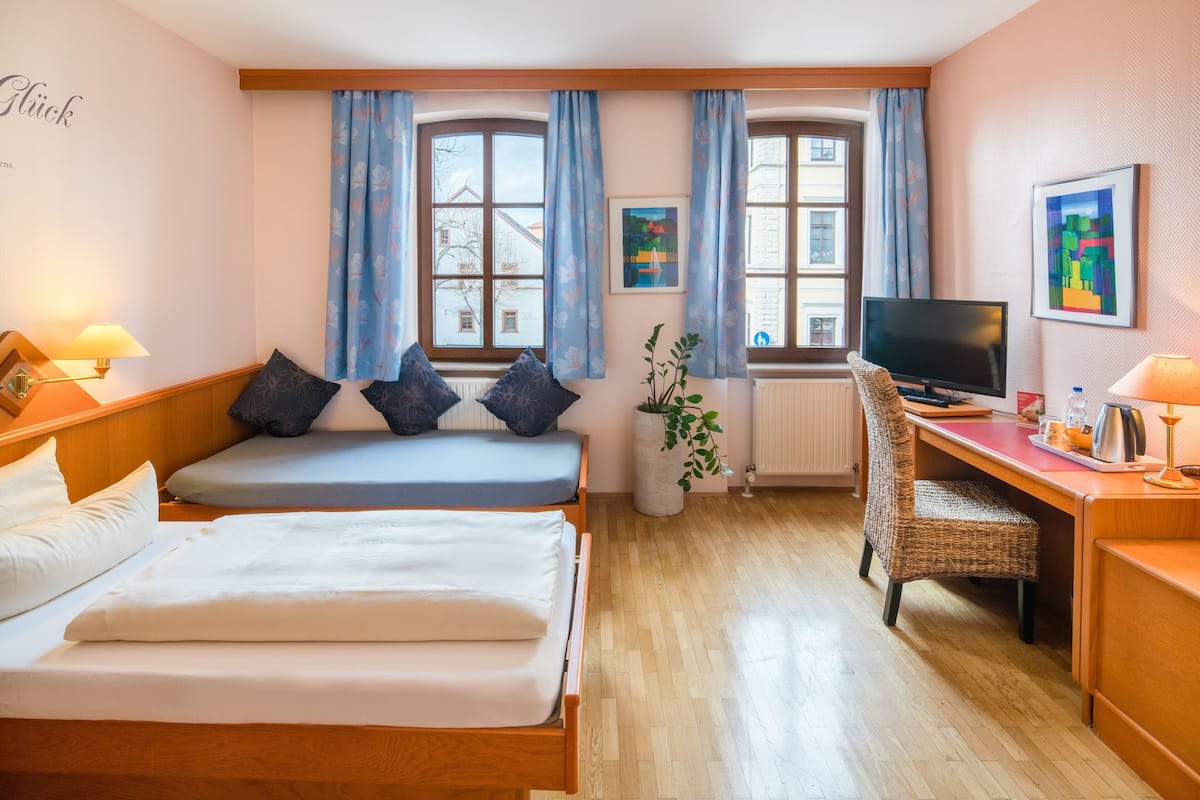 A hotel room with two beds, a desk, a television, and large windows with curtains.