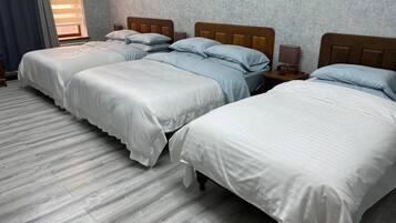 Ett hotellrum med tre enkelsängar, trägavlar och en grå vägg med en tydlig struktur.