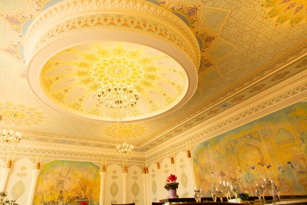 A room with ornate ceiling artwork, a chandelier, and a mural depicting historical figures.