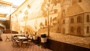 A courtyard with a mural of a castle, tables, chairs, and potted plants.