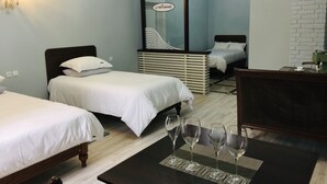 A hotel room with two single beds, a small table with wine glasses, a window with a view, and a brick wall.