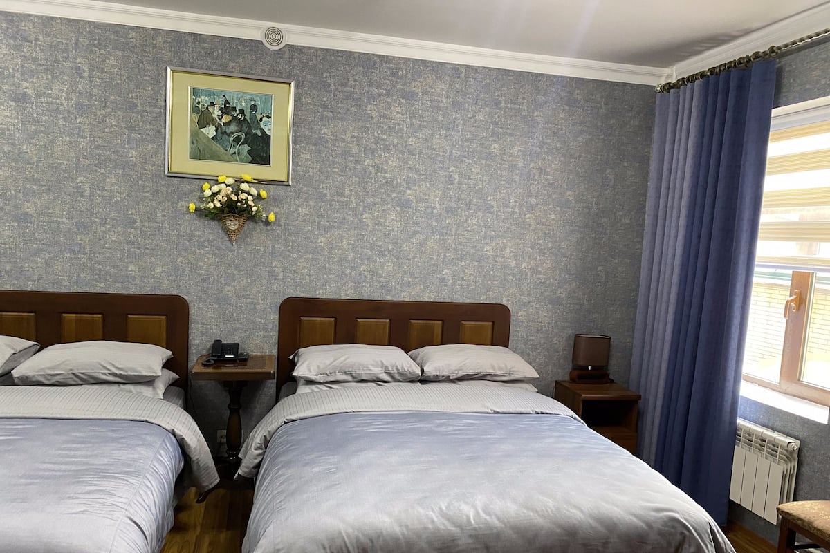 A hotel room with two beds, a nightstand, a lamp, a framed picture, and a window with curtains.
