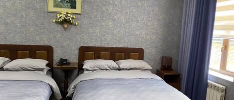 A hotel room with two beds, a nightstand, a lamp, a framed picture, and a window with curtains.