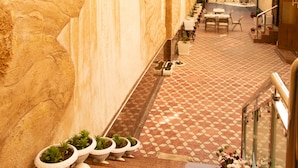 A narrow corridor with a checkered floor, potted plants, and outdoor seating.