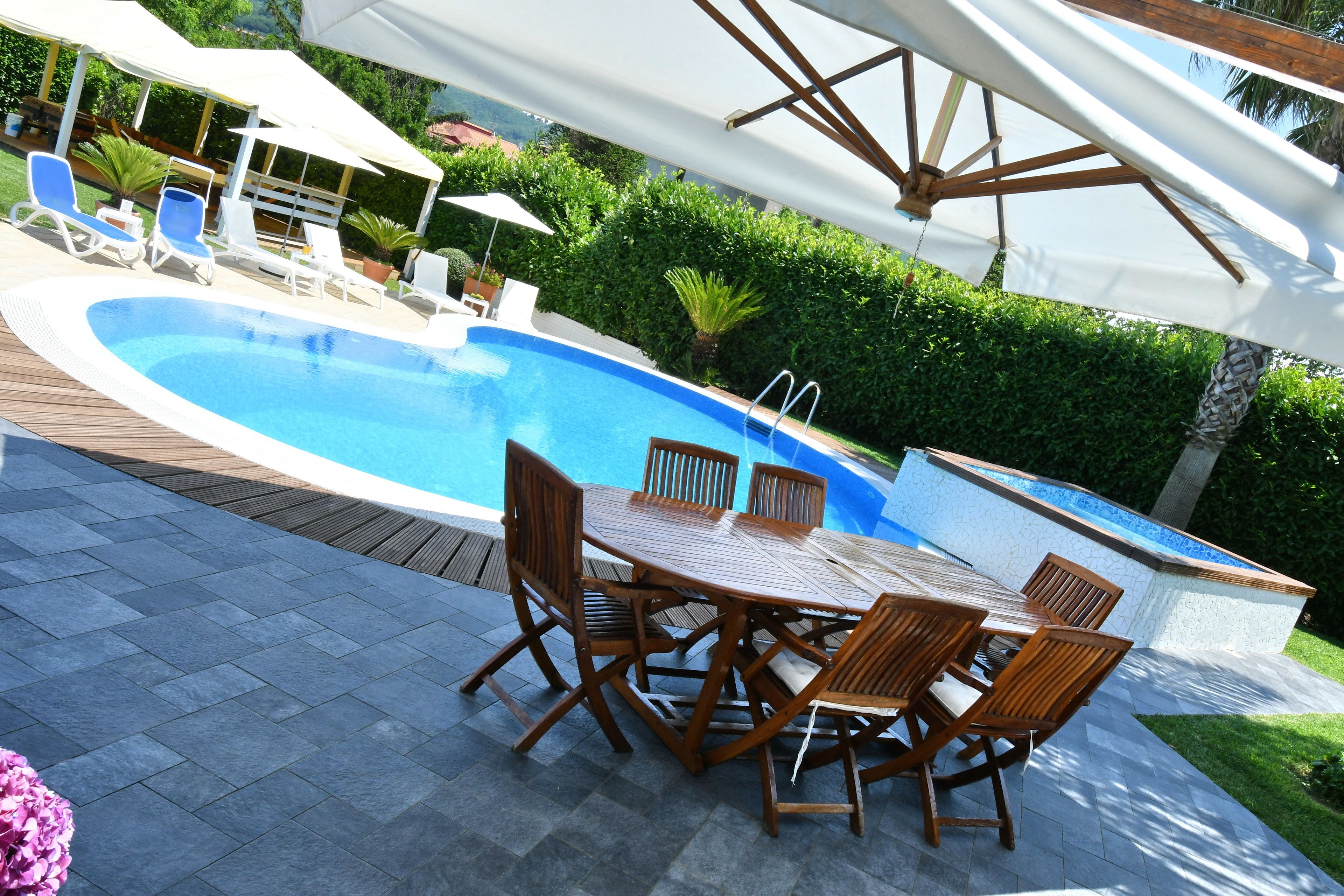 A poolside area with a wooden table and chairs, a pool, and umbrellas.