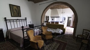 A bedroom with a bed, two armchairs, a sofa, and an archway leading to a kitchen area.