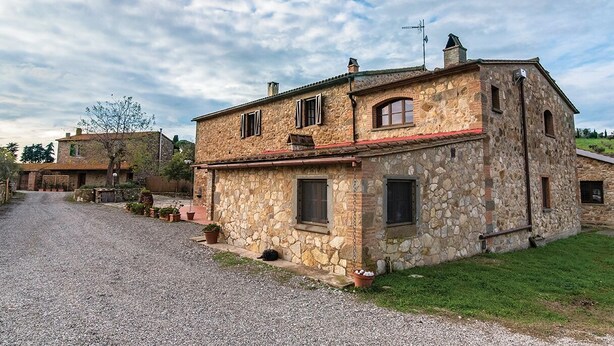 A stone house with a gravel driveway and a grassy area in front.