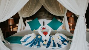 A bed with a canopy, a heart-shaped towel arrangement, and a bouquet of flowers. - Perdana Lembongan (Lembongan Island)