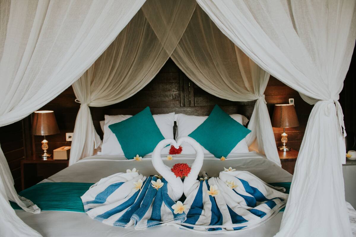 A bed with a canopy, a heart-shaped towel arrangement, and a bouquet of flowers.