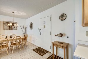 Un comedor con mesa y sillas de madera, una araña y decoración en la pared, incluyendo un reloj y una escultura de pez.
