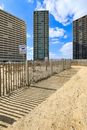 Un sendero arenoso que lleva a una zona vallada con edificios modernos al fondo.