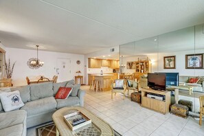 A living room with a sofa, coffee table, TV, and kitchen in the background.