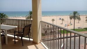 A balcony with a table and chairs, overlooking a beach with palm trees and a clear sky. - Infante E4-4º Solo Familias! (Playa de Gandía)