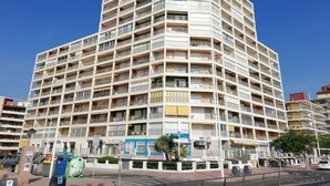 A multi-story hotel with balconies, a ground floor with shops, and a clear blue sky. - Infante E5-11º Solo Familias! (Playa de Gandía)