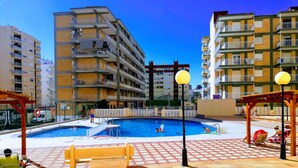 A swimming pool area with a bench, a lifeguard stand, and a view of surrounding apartment buildings. - Infante E5-11º Solo Familias! (Playa de Gandía)