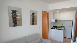 A compact living space with a sofa, a kitchenette, and a door leading to another room. - Infante E5-11º Solo Familias! (Playa de Gandía)