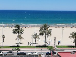 A beach with palm trees, a parking lot, and a clear view of the ocean. - Danio 5º, Solo Familias! (Playa de Gandía)
